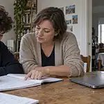 Un adolescent reprend un exercice dans son cahier avec une enseignante à la maison